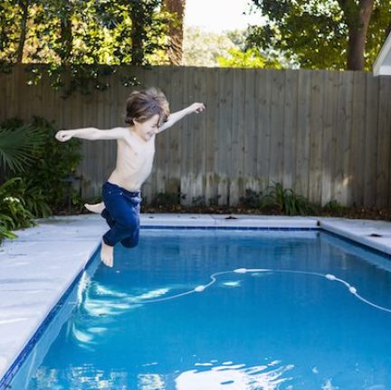 A six year old boy leaping into a swimming pool